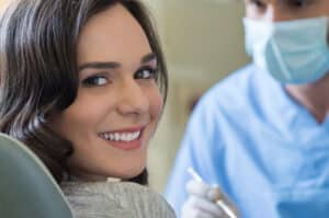 Woman looking at camera and smiling during a dental cleaning, showing off her white teeth after fluoride treatment