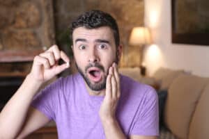 Man with a surprised expression, holding his jaw in pain with his broken tooth in his other hand.