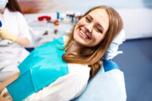 Woman smiling while getting a routine professional dental cleaning to prevent tooth loss.